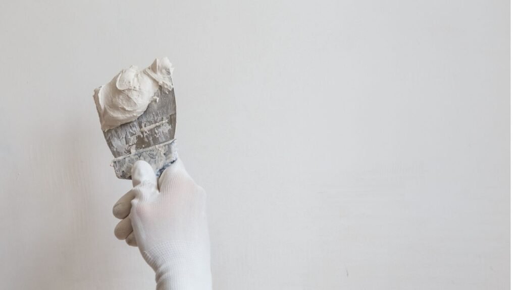 Wall Putty vs POP Punning – Which is Better for Your Walls? 3 Illustration comparing wall putty being applied on a brick wall with a putty knife and POP punning with a trowel on a tray of plaster